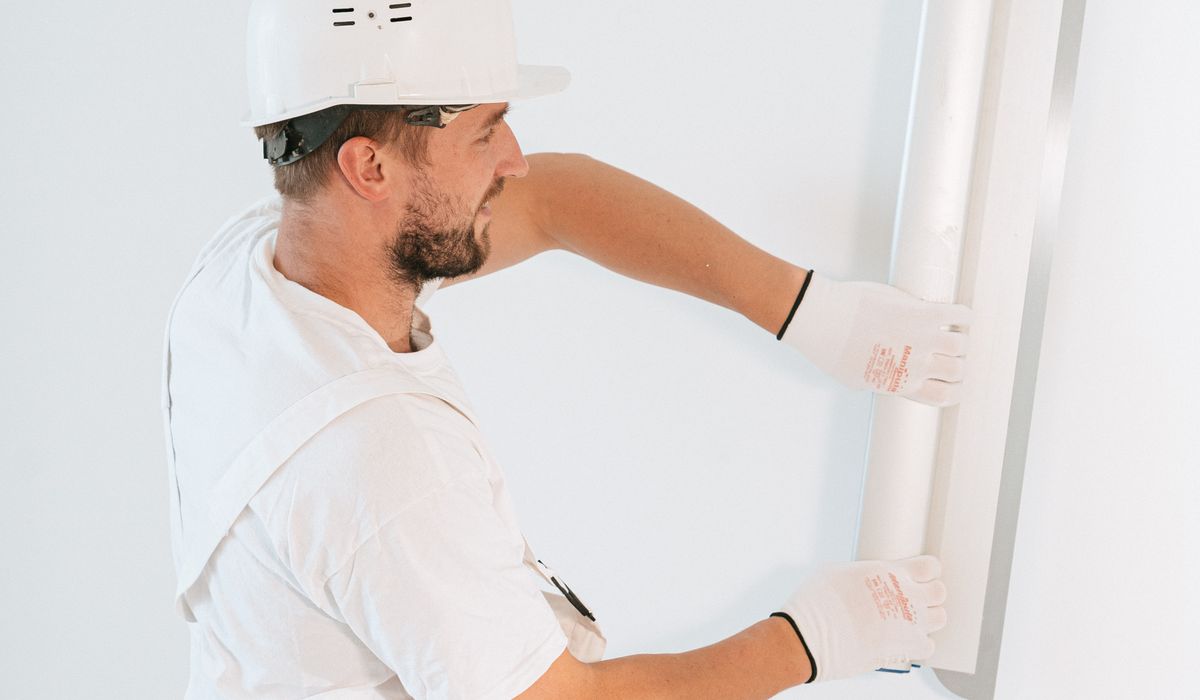 Worker in white hard hat fitting a drywall sheet against a wall