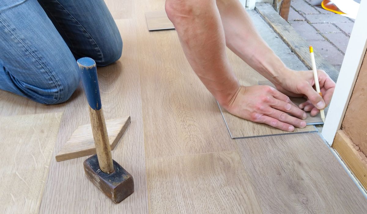 Installer marking and fitting plank flooring at a doorway