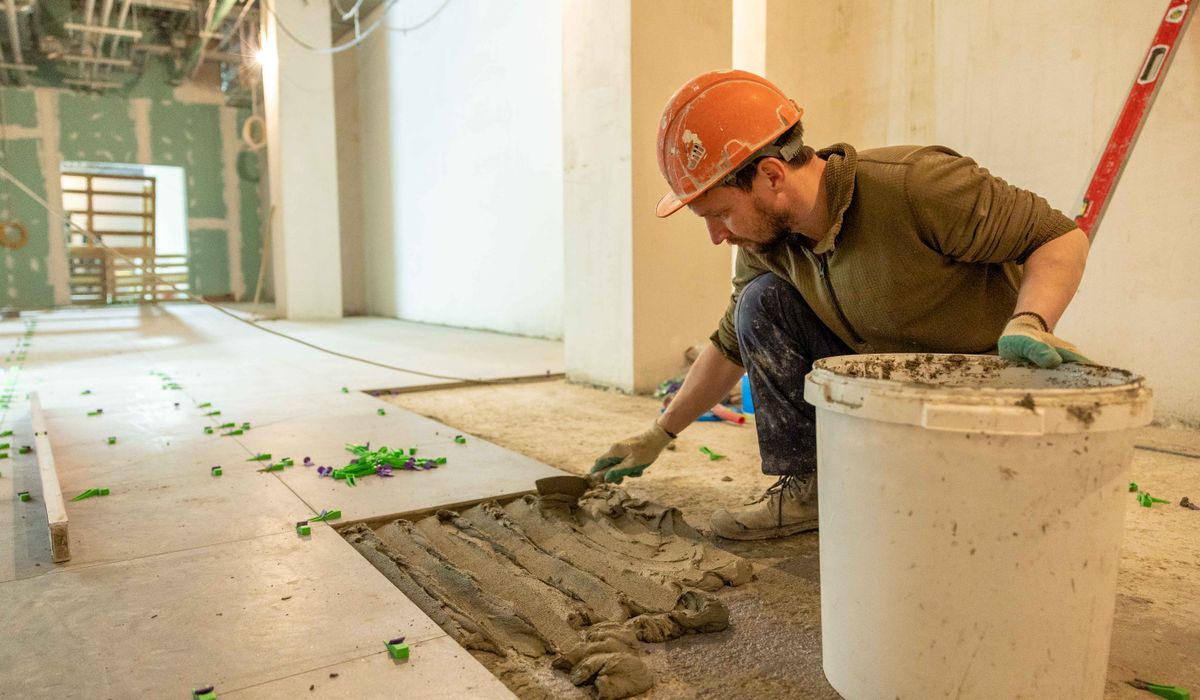 Worker in a hard hat setting floor tile into fresh thinset